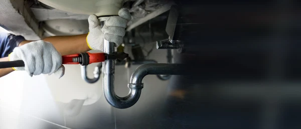 Technicien plombier utilisant une clé pour réparer une conduite d'eau sous l'évier