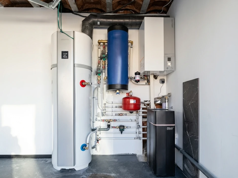 Technicien en salopette bleue installant un radiateur blanc dans une pi&egrave;ce lumineuse aux murs blancs, pr&egrave;s d'une fen&ecirc;tre