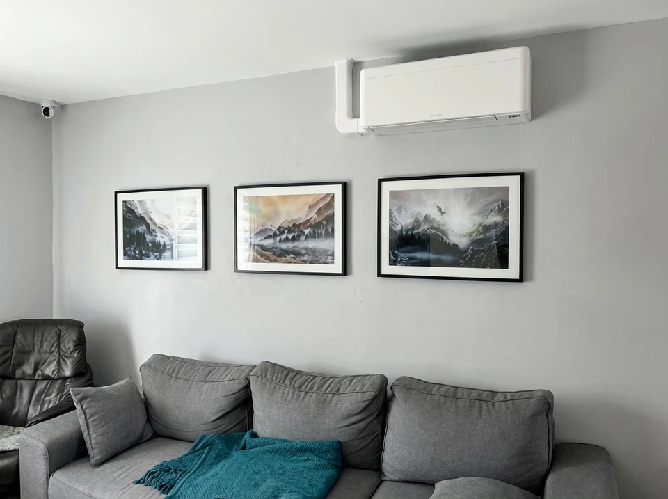 Technicien en salopette bleue installant une unité extérieure de climatisation sur mur en briques blanches, positionné sur échelle métallique